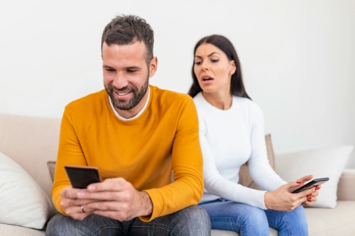 suspicious woman looking at partner's cellphone over their shoulder